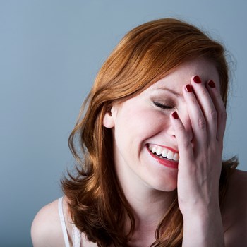 A woman laughing with her hand covering half of her face. 