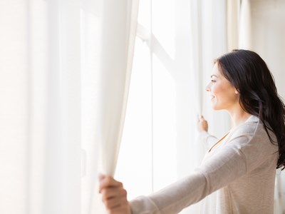 A woman holding the curtains open looking out of the window. 