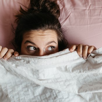 woman in bed with sheets covering part of her face