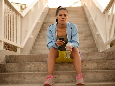 A woman sitting on steps holding a phone and a water bottle. 