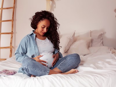 pregnant woman sitting on a bed with her hands on her belly. 