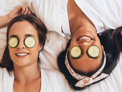 two women laying down with cucumber slices over their eyes
