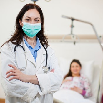 doctor in a patients room with a mask on looking at the camera