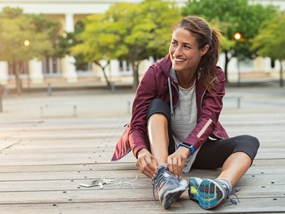 A woman in workout clothing sitting on the ground adjusting her shoe. 