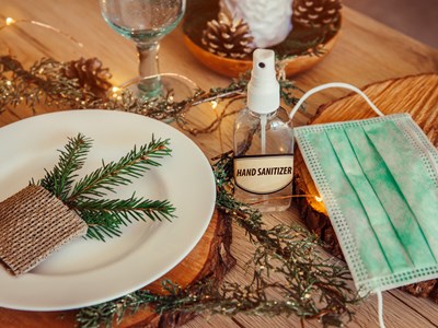 A close-up of a dinner table at the holidays with hand sanitizer and a mask on the table. 