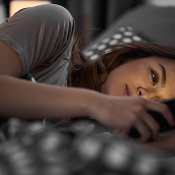 a woman laying in bed looking at her phone