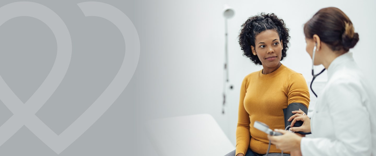 A doctor checking a woman's blood pressure with a blood pressure cuff and stethoscope. 