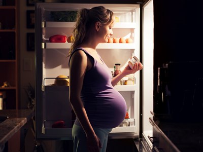 A pregnant woman standing in front of the refrigerator looking at yogurt ingredients.