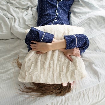 a woman laying on a bed hugging a pillow that is covering her face