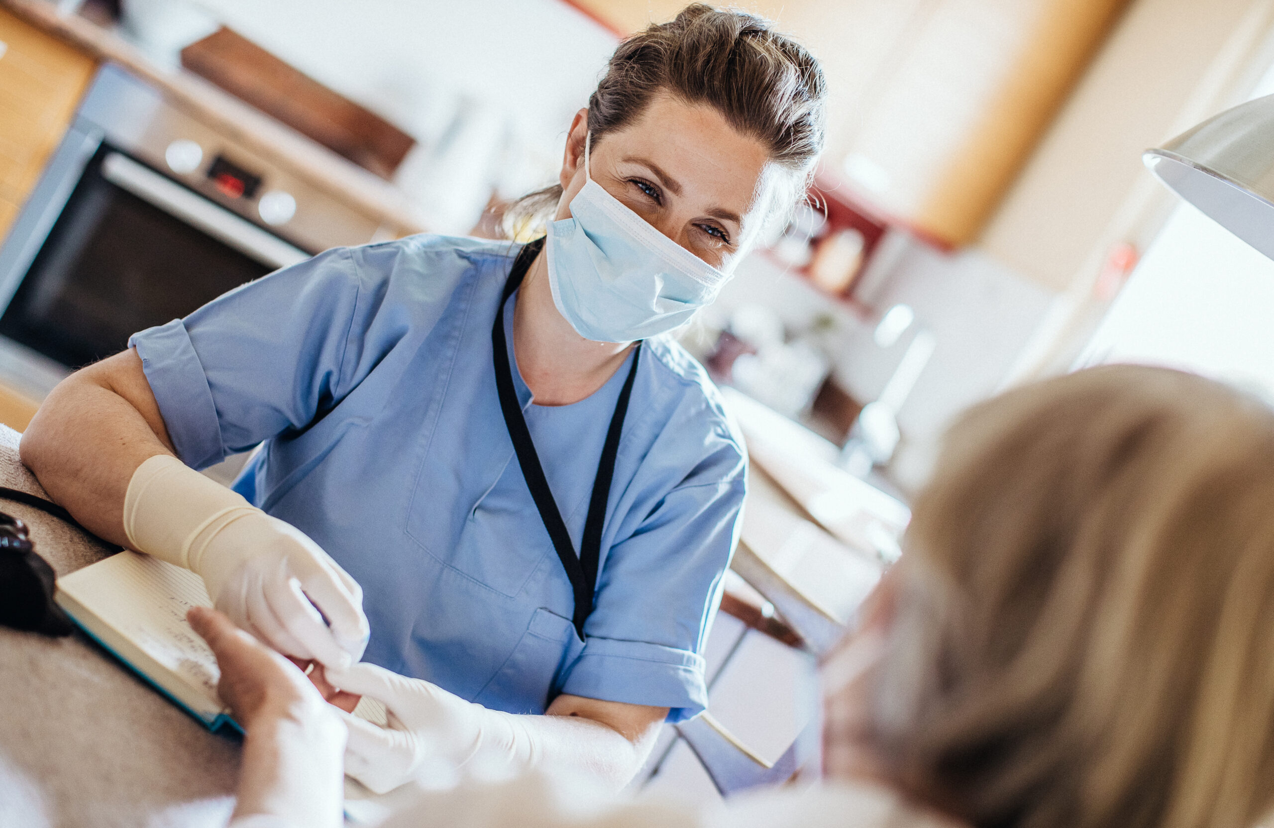 A nurse wearing a face mask while treating a person in their kitchen.