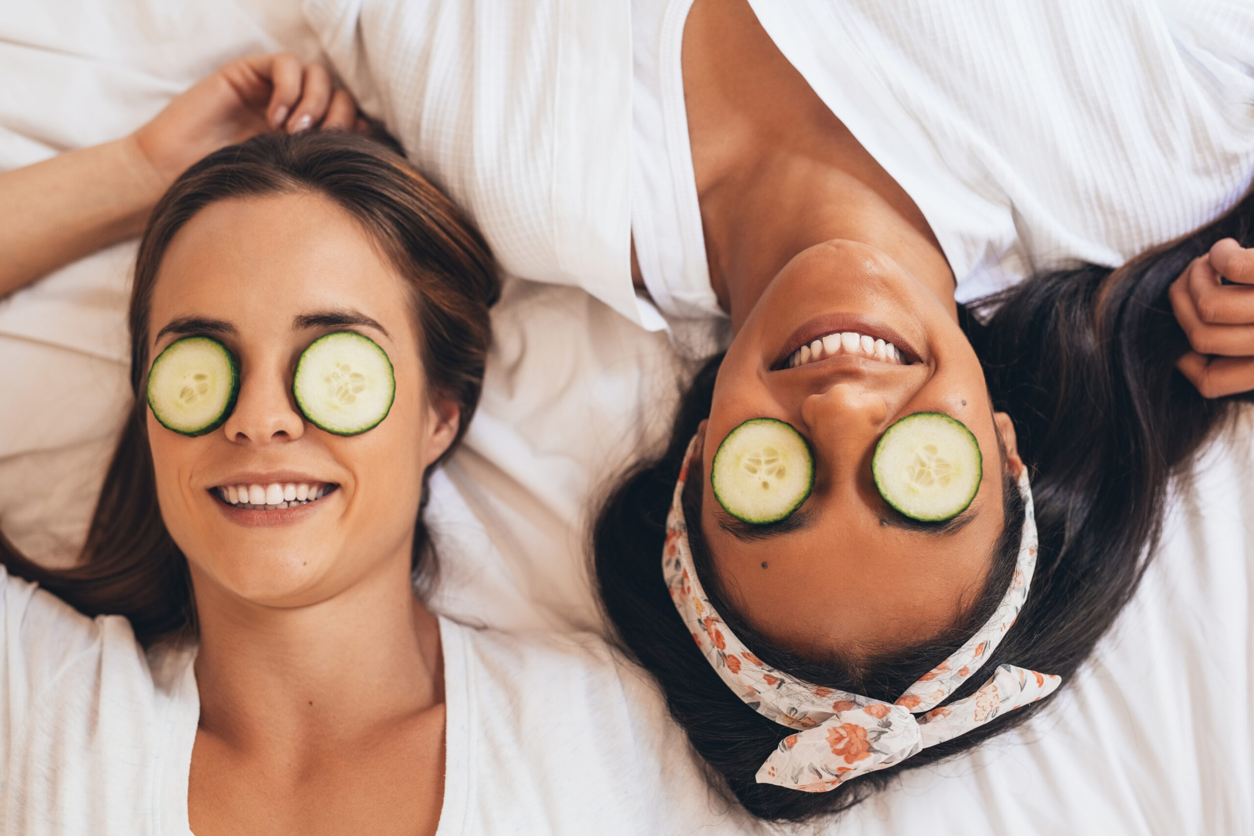 two women laying down with cucumber slices over their eyes