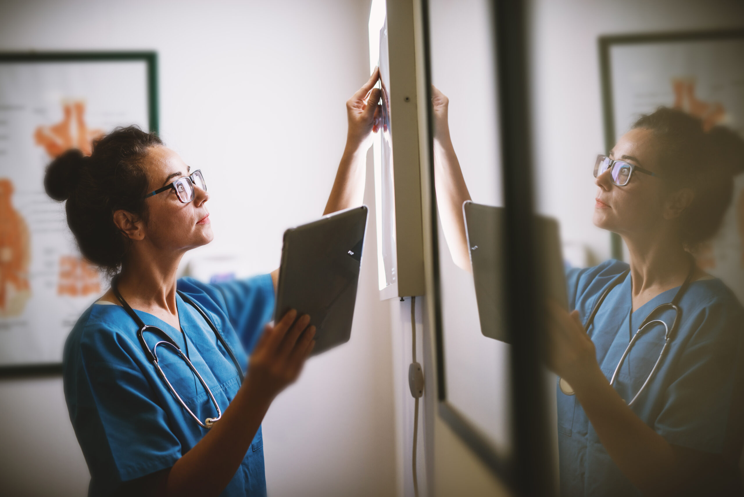 A doctor looking at results on a light board while holding an iPad.