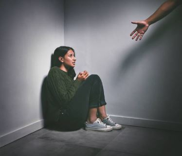 woman sitting in a dark corner with a hand reaching to help