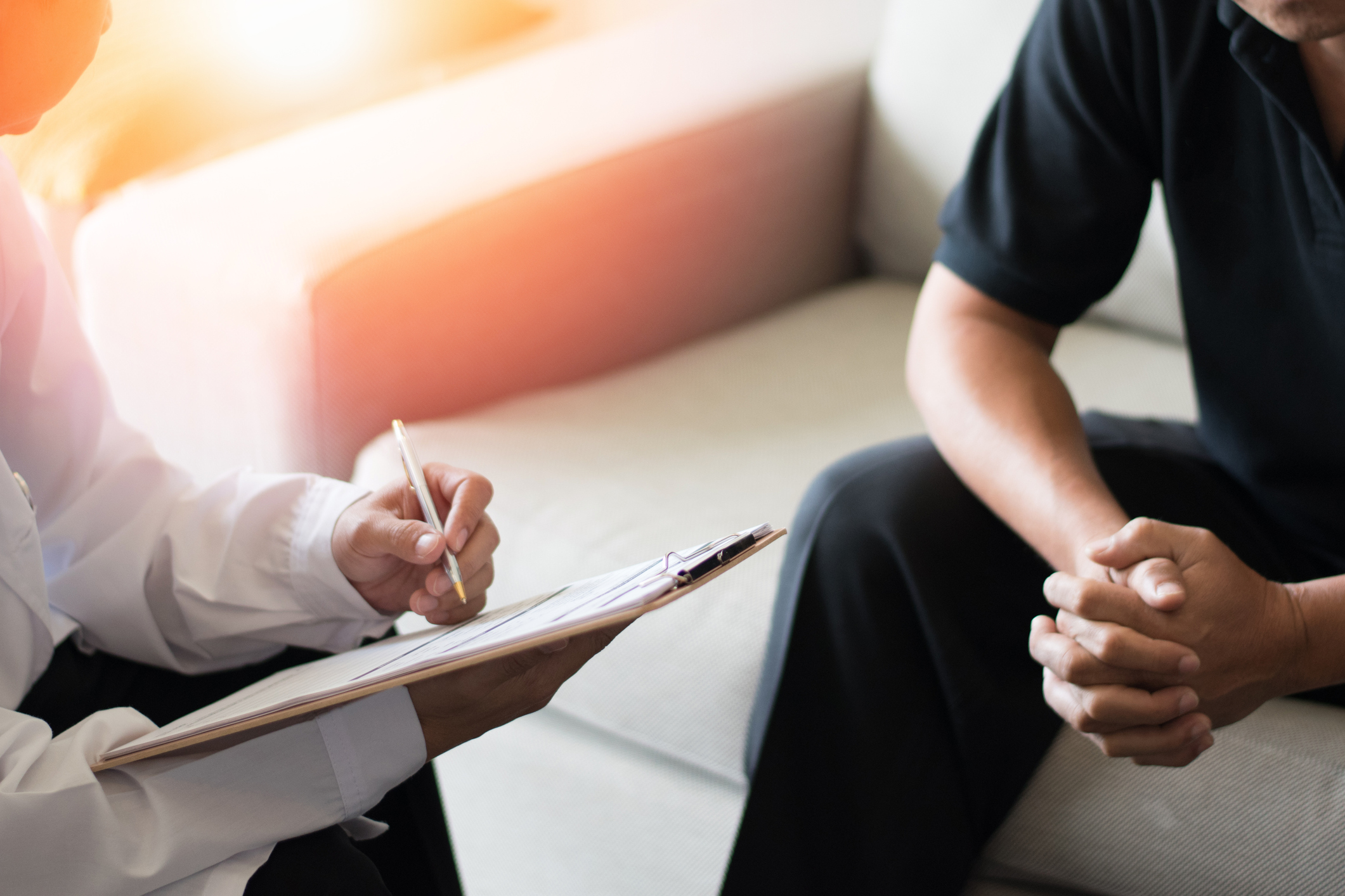 A close-up shot of a doctor taking notes talking with a male patient.