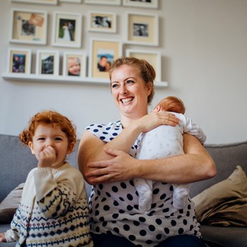 a mother, toddler and infant smiling while looking off camera