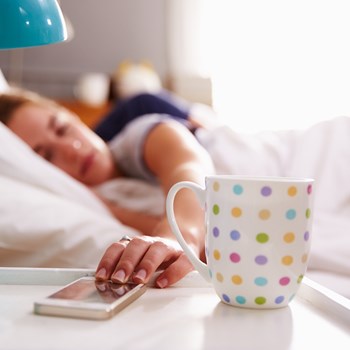 woman in bed reaching for her phone on nightstand