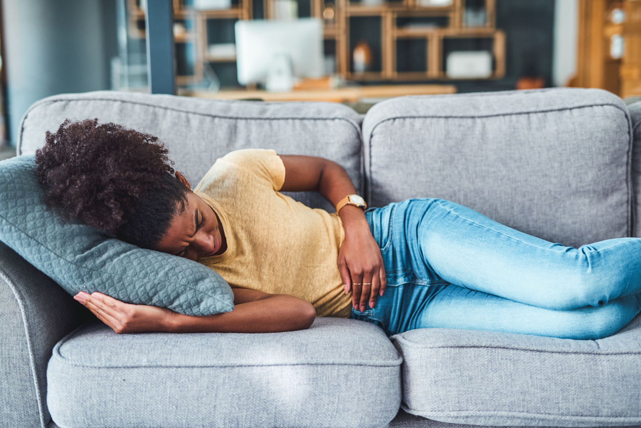 woman on couch holding her stomach in pain