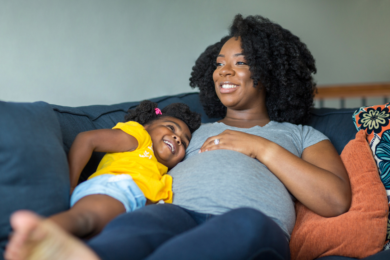 A pregnant woman and her daughter lying on the couch.