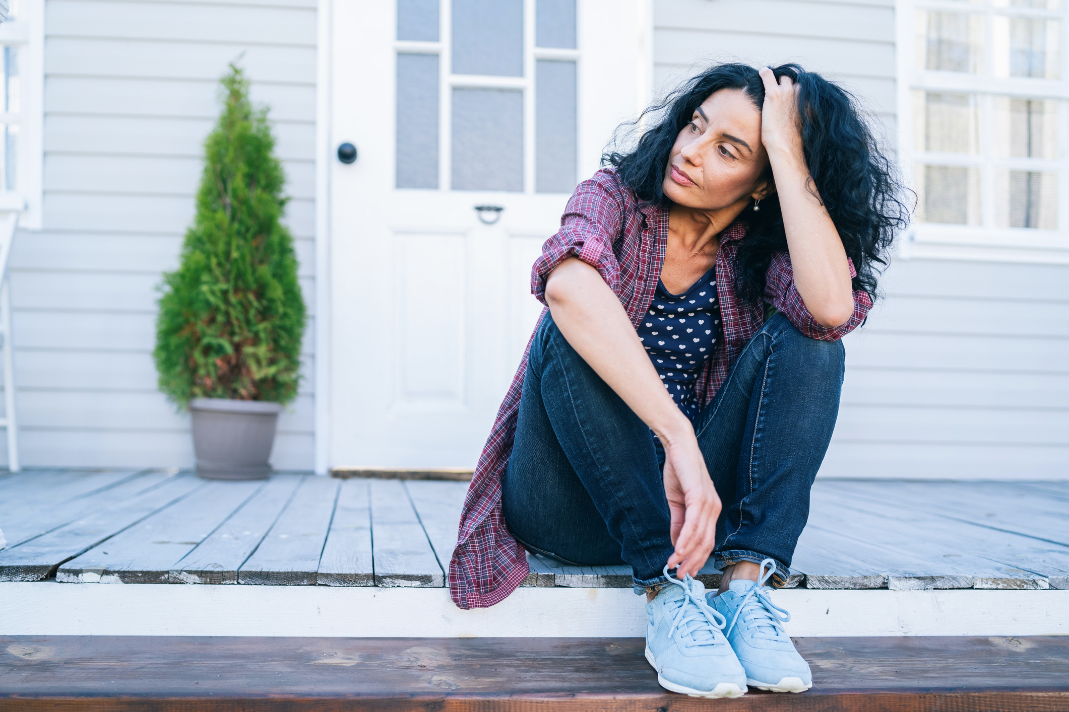 A woman sitting on her front porch with her hand in her hair looking off into the distance.