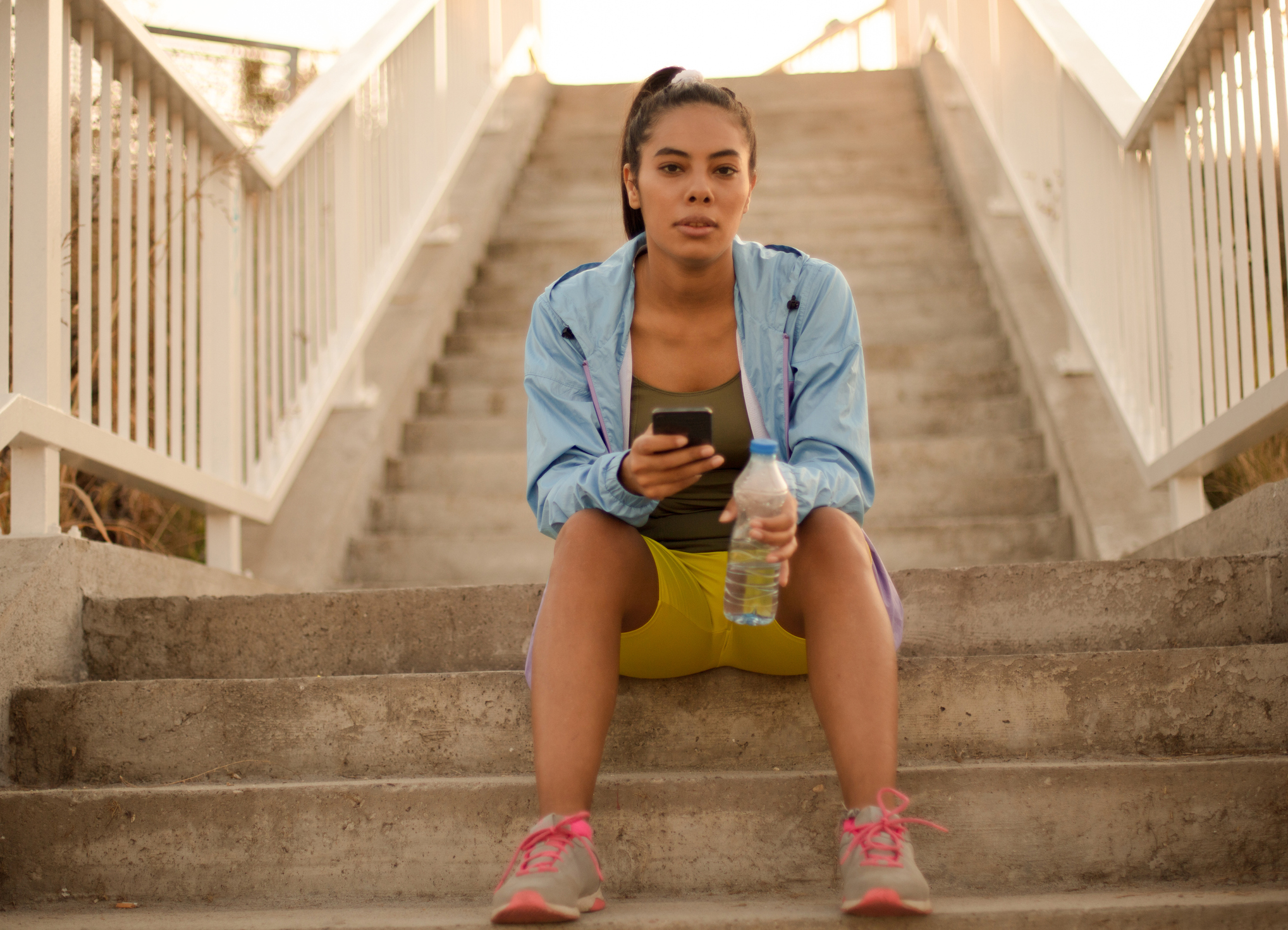 A woman sitting on steps holding a phone and a water bottle.