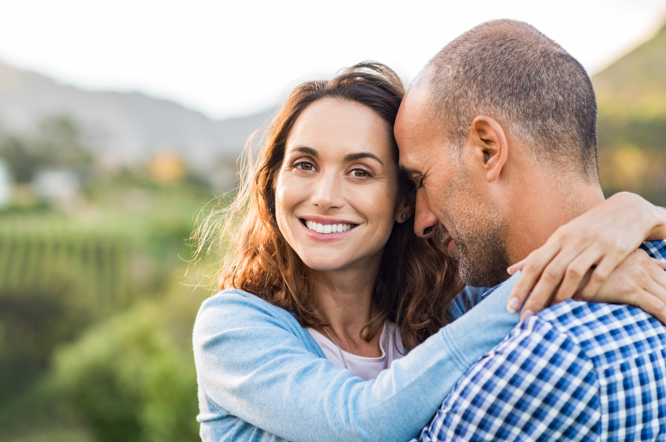 A woman looking at the camera with her arms around a man's neck.