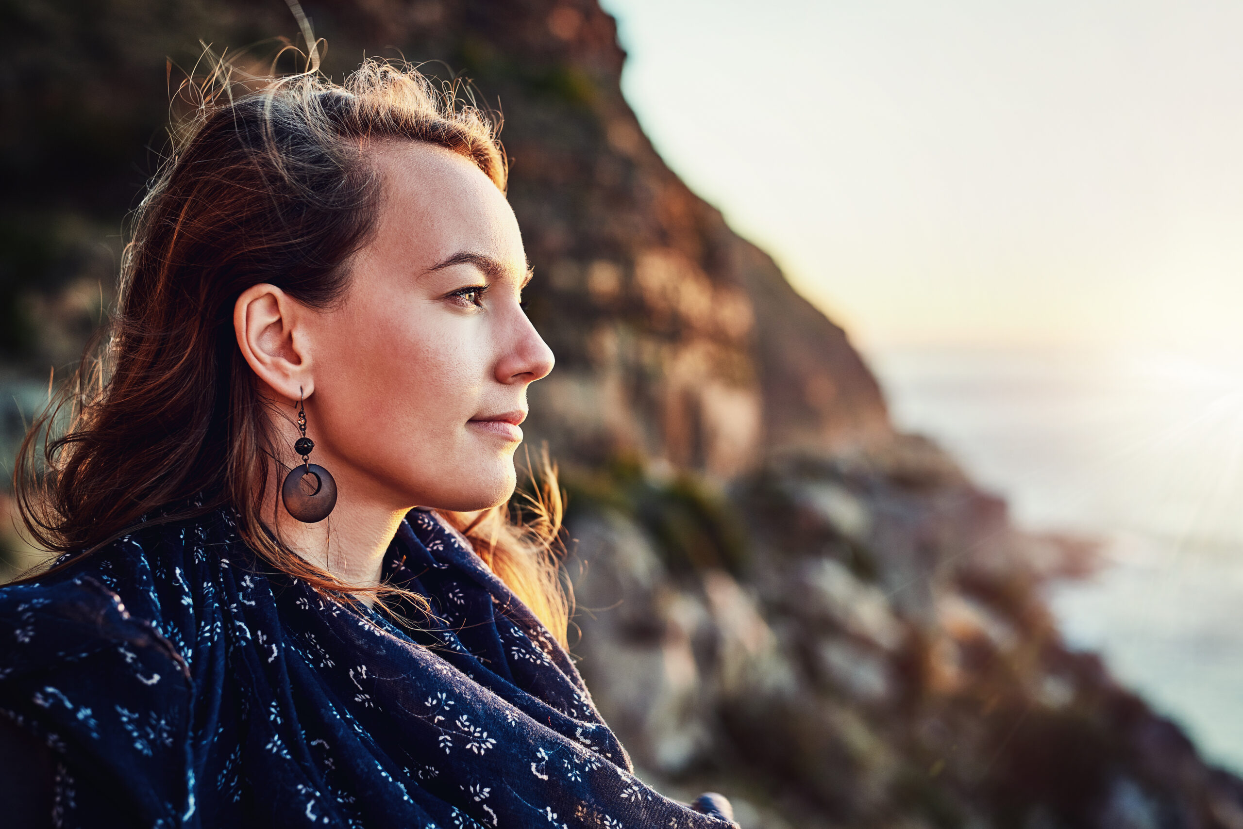 A woman looking off into the distance while sitting on the side of a mountain.