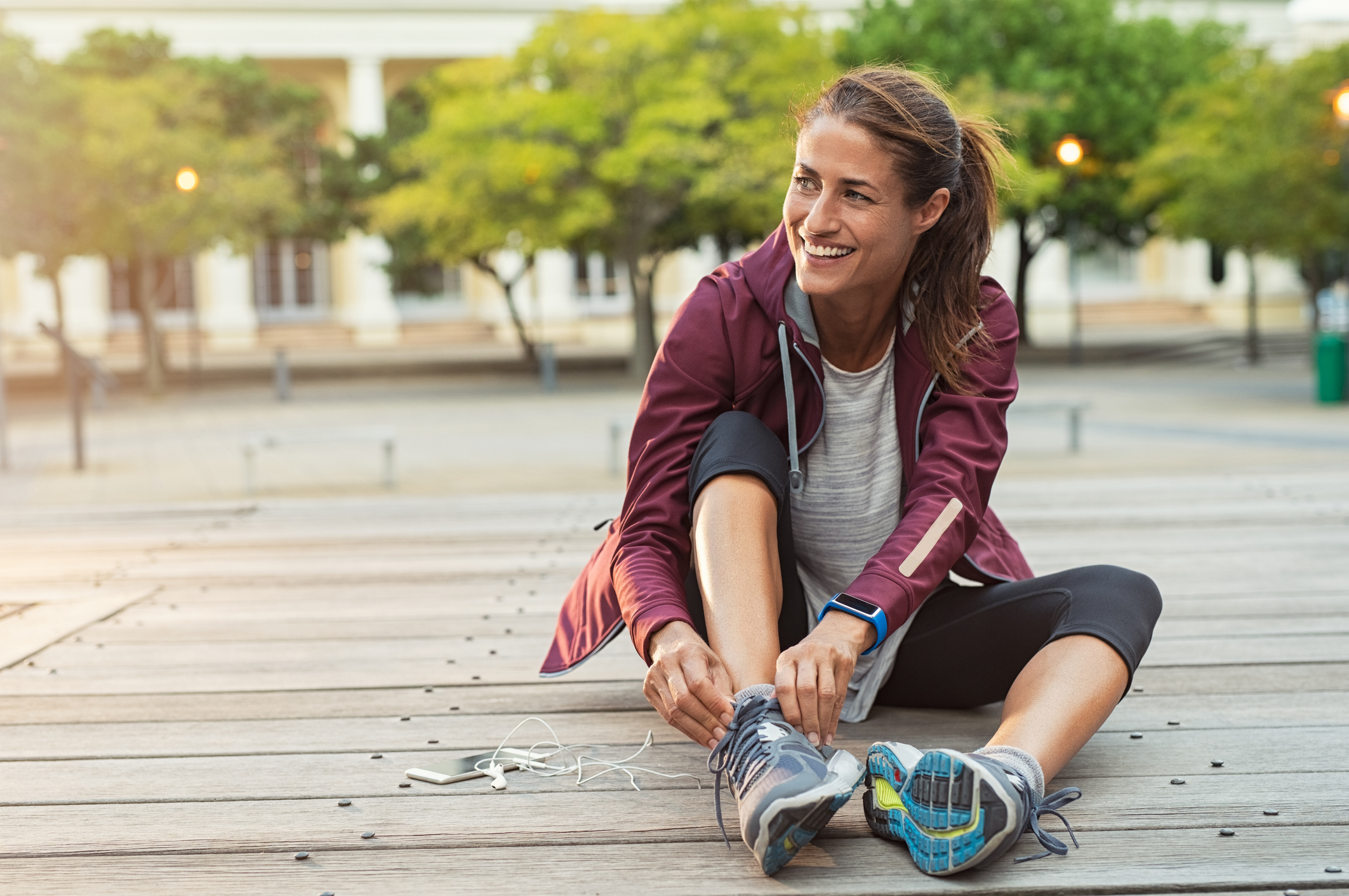 A woman in workout clothing sitting on the ground adjusting her shoe.