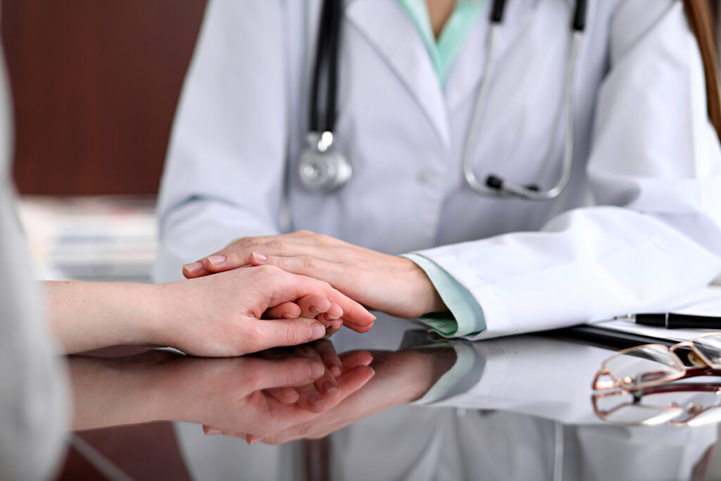 A close-up of a doctor holding a patient's hand in comfort.