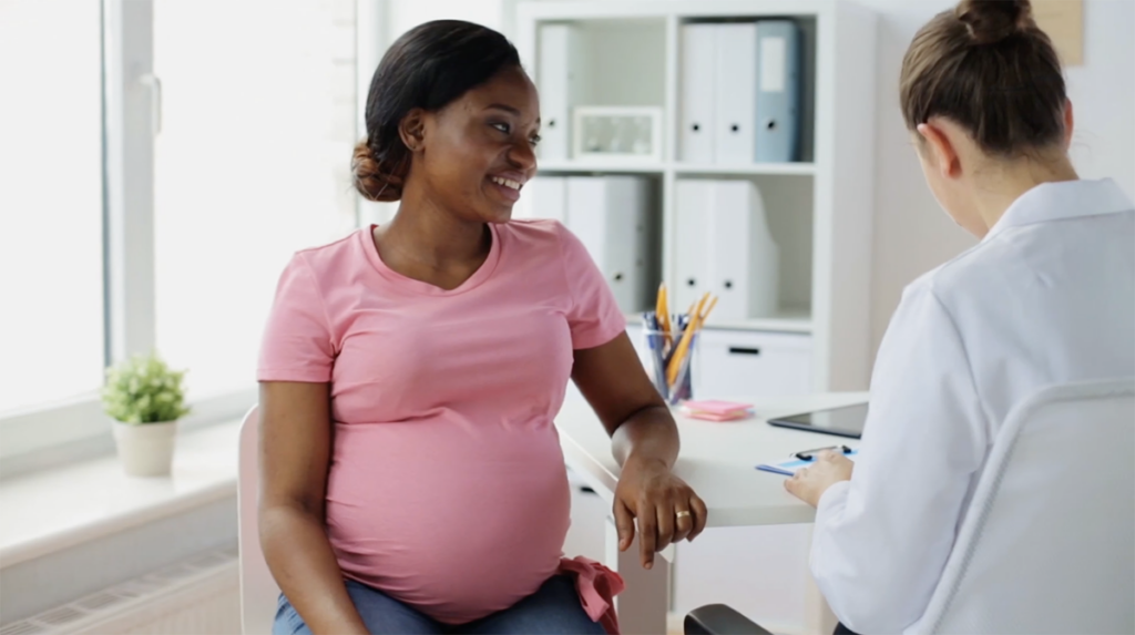 A pregnant woman sitting in a doctor's office talking.