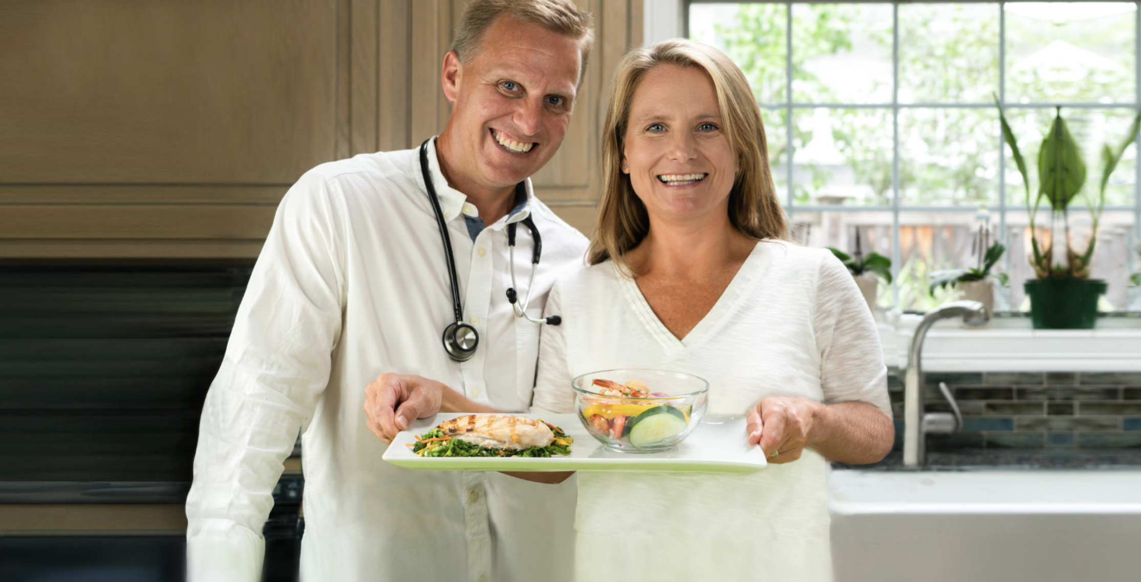 A doctor and patient standing in front of the camera holding a tray of healthy food.