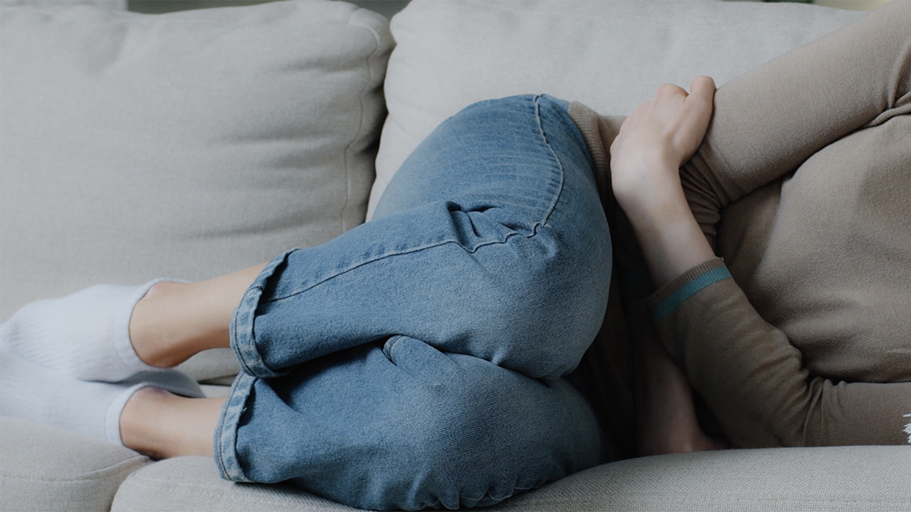 Woman laying on her side holding stomach in discomfort.