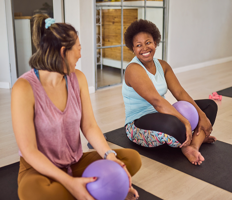 women on a yoga mat holding a ball having a good time